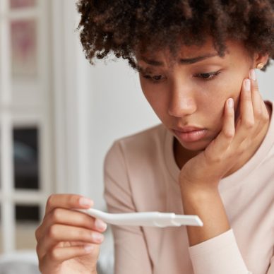 Displeased frustrated African American woman looks stressfully at pregnancy test, finds out she will become mother, looks desperately at result. Close up shot of young lady has problems with fertility