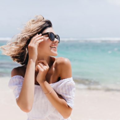 Relaxed short-haired woman posing on sea background. Outdoor shot of blithesome young lady in sunglasses enjoying vacation.