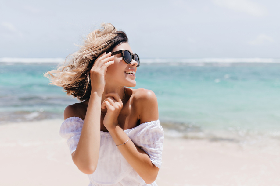 Relaxed short-haired woman posing on sea background. Outdoor shot of blithesome young lady in sunglasses enjoying vacation.