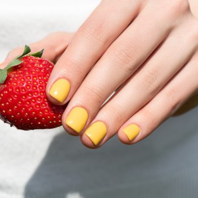 Close up of female hand with pretty yellow nail design manicure holding ripe strawberry