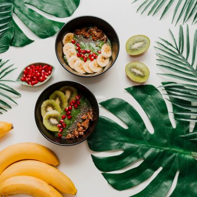 Acai bowl with healthy berries, kiwi, avocado  on tropical palm leaf on white background. Healthy vegetarian food.