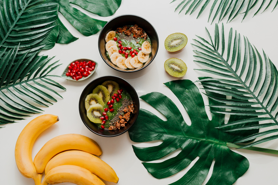 Acai bowl with healthy berries, kiwi, avocado  on tropical palm leaf on white background. Healthy vegetarian food.