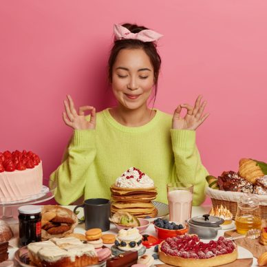 Beautiful Asian woman sweet tooth meditates and practices yoga, eats yummy pancakes and cakes, feels relaxed, going to taste birthday cake, loves desserts, gets much calories. Junk food concept