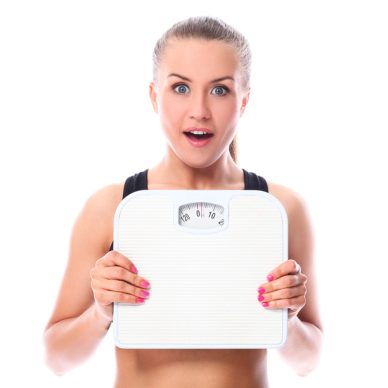 Beautiful fitness girl holding scales over white background