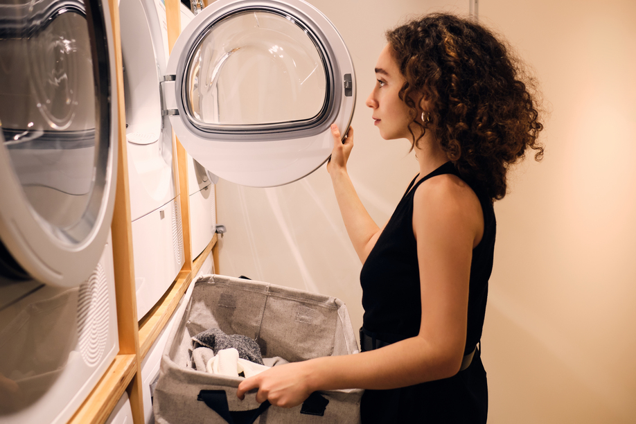 Beautiful girl loading clothes into washing machine in self-service laundry