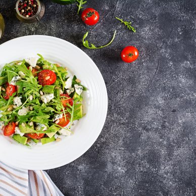 Dietary salad with tomatoes, blue cheese, avocado, arugula and pine nuts. Top view. Flat lay.