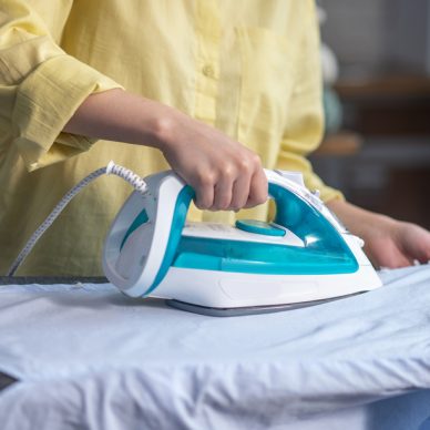 Cropped photo of a woman smoothing out wrinkles on the shirt with a steam iron