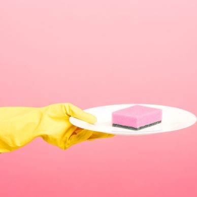 Hands in yellow protective gloves and a plate against rose background. cleaning concept
