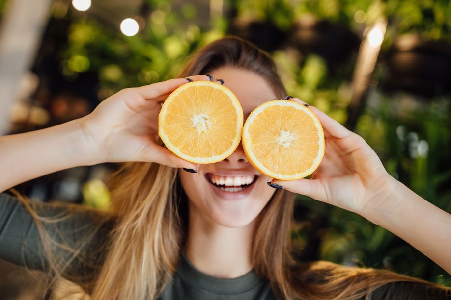 Happy young caucasian woman holding fresh oranges in front of eyes and smiling.