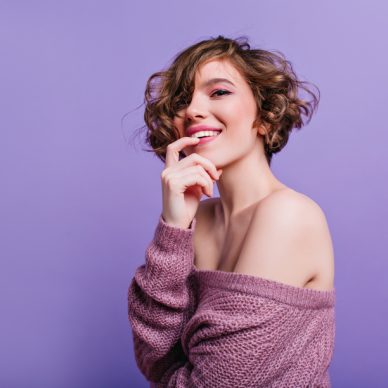 Happy young woman playfully posing on purple background. Beautiful european girl with shiny brown short hair smiling to camera.