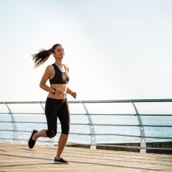 Picture of young attractive fitness girl running with sea on background