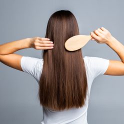 Rear view of Combing healthy long straight female hair isolated on gray background