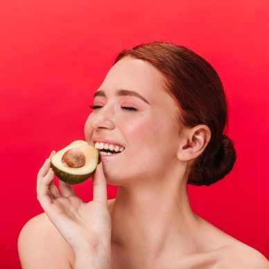 Refined girl eating avocado. Studio shot of enchanting caucasian woman posing on red background.