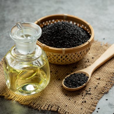Sesame oil and raw black sesame seeds on dark background