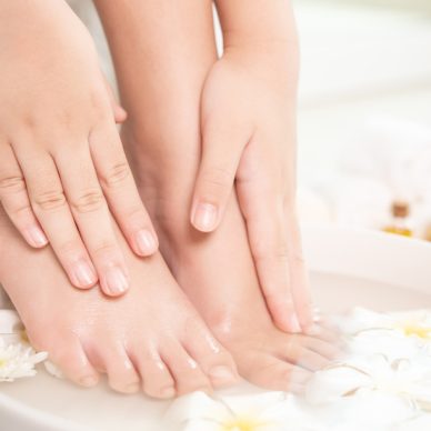 closeup view of woman soaking her hand and feet in dish with water and flowers on wooden floor. Spa treatment and product for female feet and hand spa. white flowers in ceramic bowl.