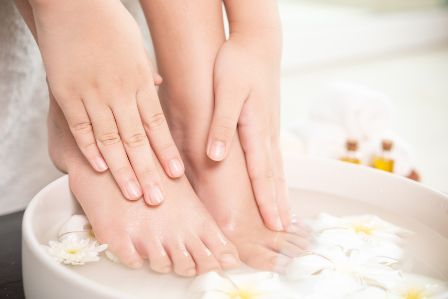 closeup view of woman soaking her hand and feet in dish with water and flowers on wooden floor. Spa treatment and product for female feet and hand spa. white flowers in ceramic bowl.