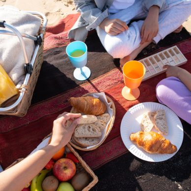 Top view of African American family on picnic on beach. Mother and children in casual clothes sitting on blanket, eating bread, drinking juice. Family, relaxation, nature concept