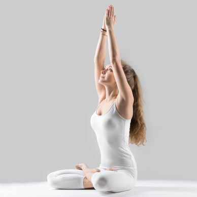 Young attractive woman practicing yoga, sitting in Padmasana exercise, Lotus pose, working out, wearing sportswear, white tank top, pants, indoor full length, isolated against grey studio background