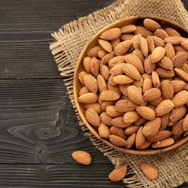 almond in a wooden bowl. on a wooden background, near a bag from burlap. Healthy food and snack, organic vegetarian food. (selective focus; close-up shot)