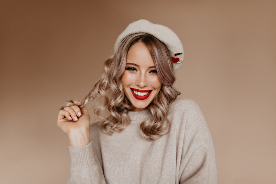Appealing french lady playing with her long hair. Wonderful white girl in brown beret smiling to camera