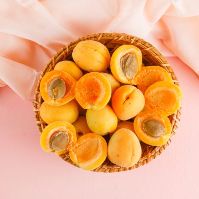 Apricots in a wicker basket on pink and textile background. flat lay.