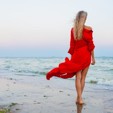 beautiful free woman in red dress in wind on sea beach walking on summer, fashion style, long legs