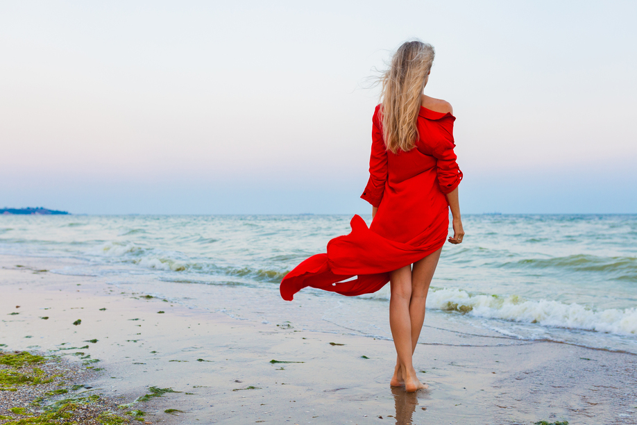beautiful free woman in red dress in wind on sea beach walking on summer, fashion style, long legs