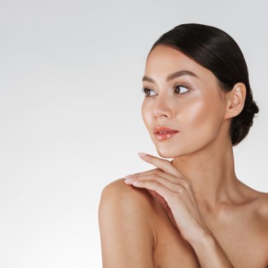 Beauty portrait of feminine young woman looking away and touching her nude shoulder isolated over white background