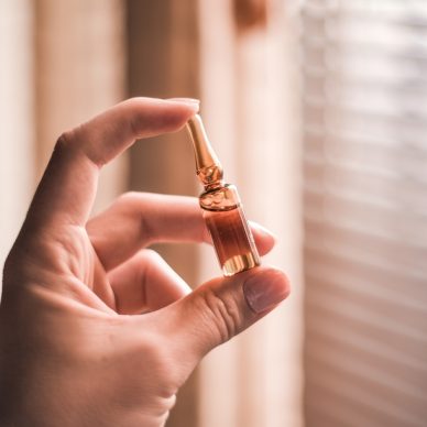 A closeup of a hand holding an ampoule under the sunlight with a window on the blurry background