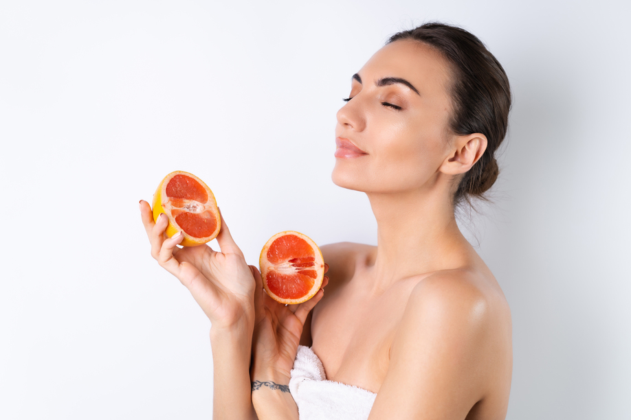 Close-up portrait of topless woman with perfect skin and natural make-up, full nude lips, holding fresh citrus vitamin C grapefruit