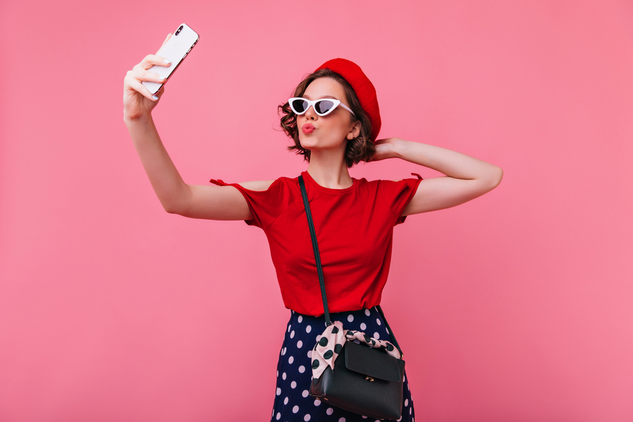 Confident french woman posing with kissing face expression. Studio shot of lovely female model in red beret expressing love while making selfie.