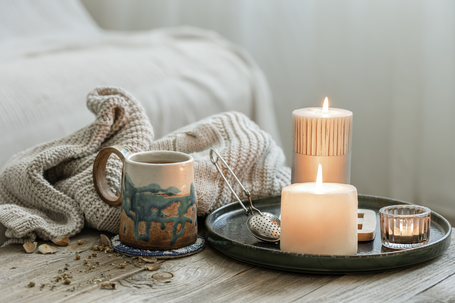 Cozy composition with a ceramic cup, candles and a knitted element on a blurred background.