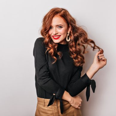 Fashionable curly woman in golden earrings standing on white background. Adorable stylish girl laughing in studio.