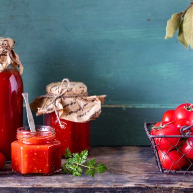 Homemade tomato ketchup made from ripe red tomatoes in glass jars with ingredients on an old wooden table