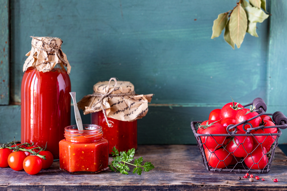 Homemade tomato ketchup made from ripe red tomatoes in glass jars with ingredients on an old wooden table