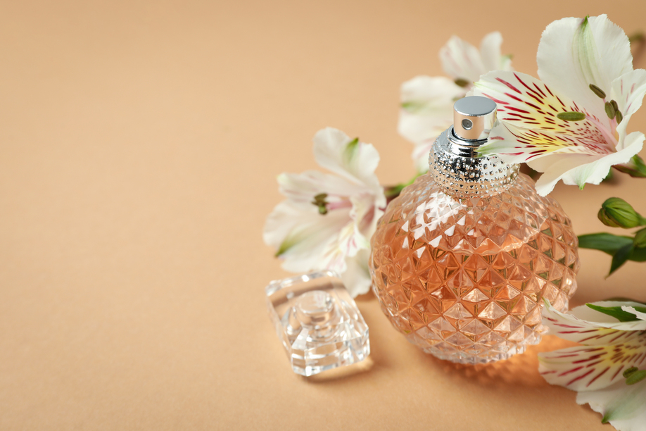 Perfume and flowers on beige background, space for text