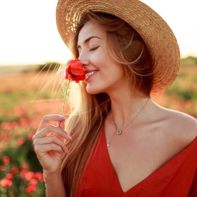 Romantic  blonde woman with flower in hand walking in amazing poppy field. Warm   sunset colors. Straw hat. Red dress. Soft colors.