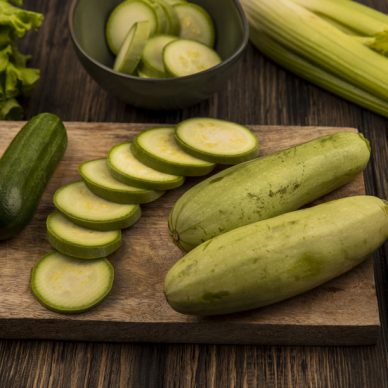 top view of fresh chopped cucumbers and zucchinis isolated on a wooden kitchen board with lettuce celery and cauliflower isolated on a wooden background