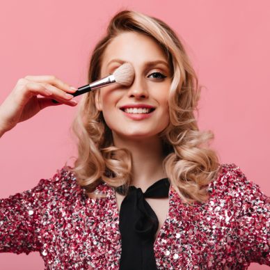 Portrait of girl with wavy hair covering her eye with makeup brush
