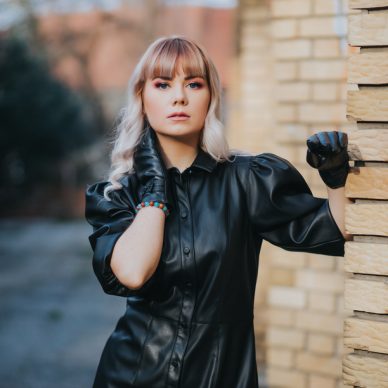 An attractive Caucasian blonde female wearing a stylish leather dress posing for a fashion photoshoot