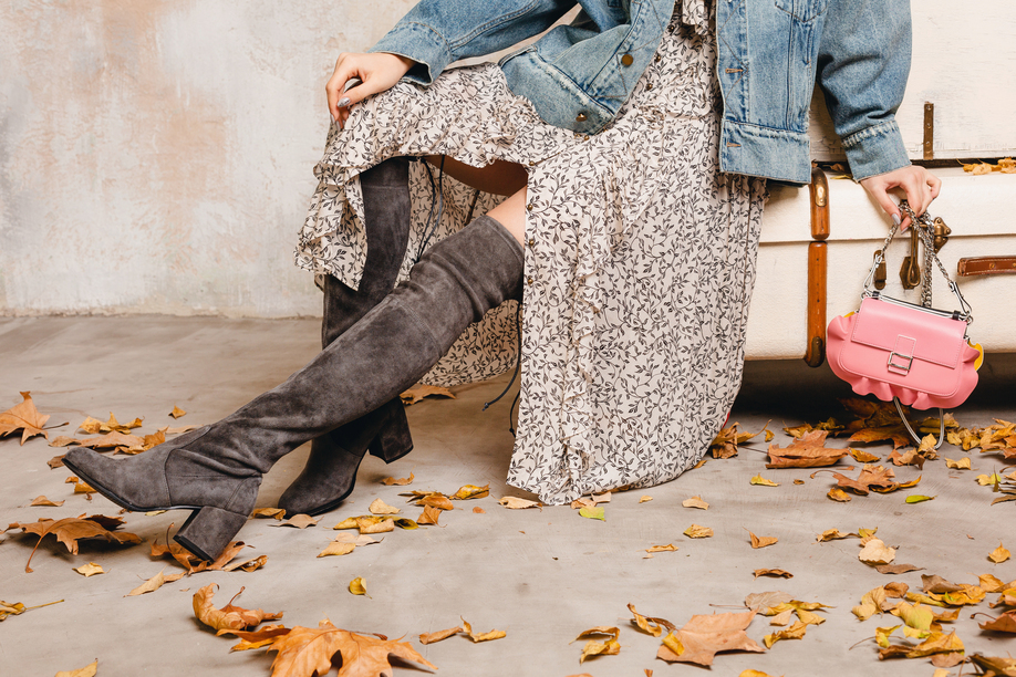 close up legs in high suede boots of stylish woman in jeans jacket against wall in street, autumn leaves, fashion trend, wearing dress, pink purse, vintage suitcases, urban style, footweartrend