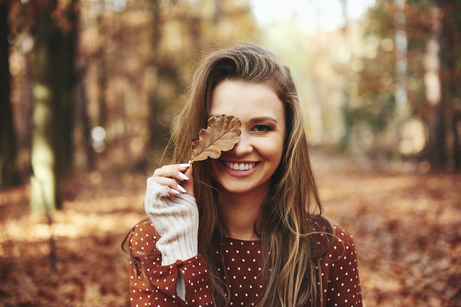 Beautiful woman covering eye with autumnal leaves