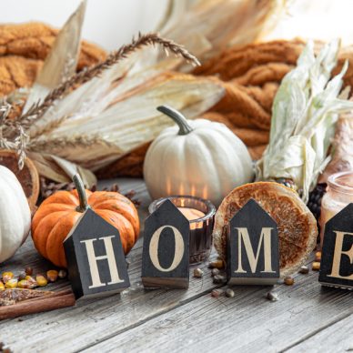 Cozy autumnal composition with decorative word home, candles, pumpkins, corn on a wooden surface in a rustic style.
