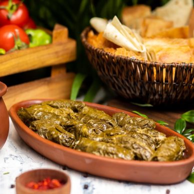 Dolma (tolma, sarma) - stuffed grape leaves with rice and meat. On kitchen table with yogurt, bread, vegetables. Traditional Caucasian, Ottoman, Turkish and Greek cuisine - Image