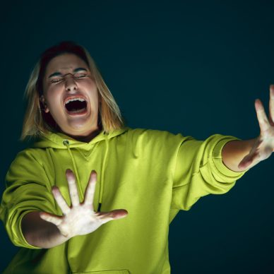 Close up portrait of young crazy scared and shocked caucasian woman isolated on dark background. Copyspace for ad. Bright facial expression, human emotions concept. Looking horror on TV, cinema.