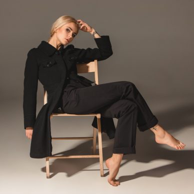 Beauty blond woman  in a black coat on chair on a gray background