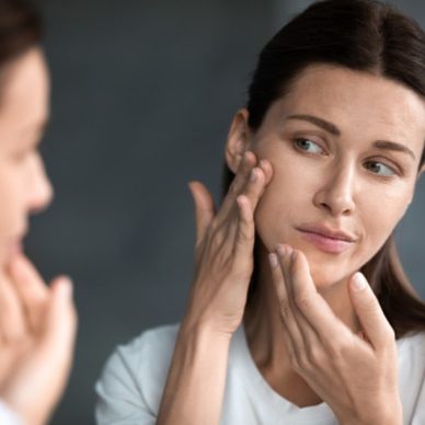 Close up unhappy sad woman looking at red acne spots on chin in mirror, upset young female dissatisfied by unhealthy skin, touching, checking dry irritated face skin, skincare and treatment concept