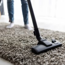 people, housework and housekeeping concept – close up of woman with legs vacuum cleaner cleaning carpet at home