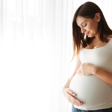 Portrait of a happy pregnant woman touching her belly while standing indoors
