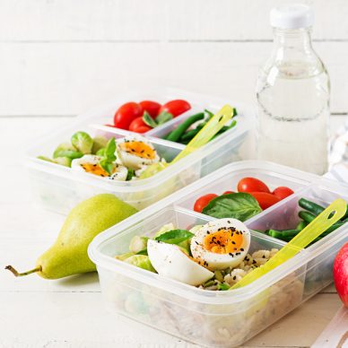 Vegetarian meal prep containers with eggs, brussel sprouts, green beans and tomato. Dinner in lunch box